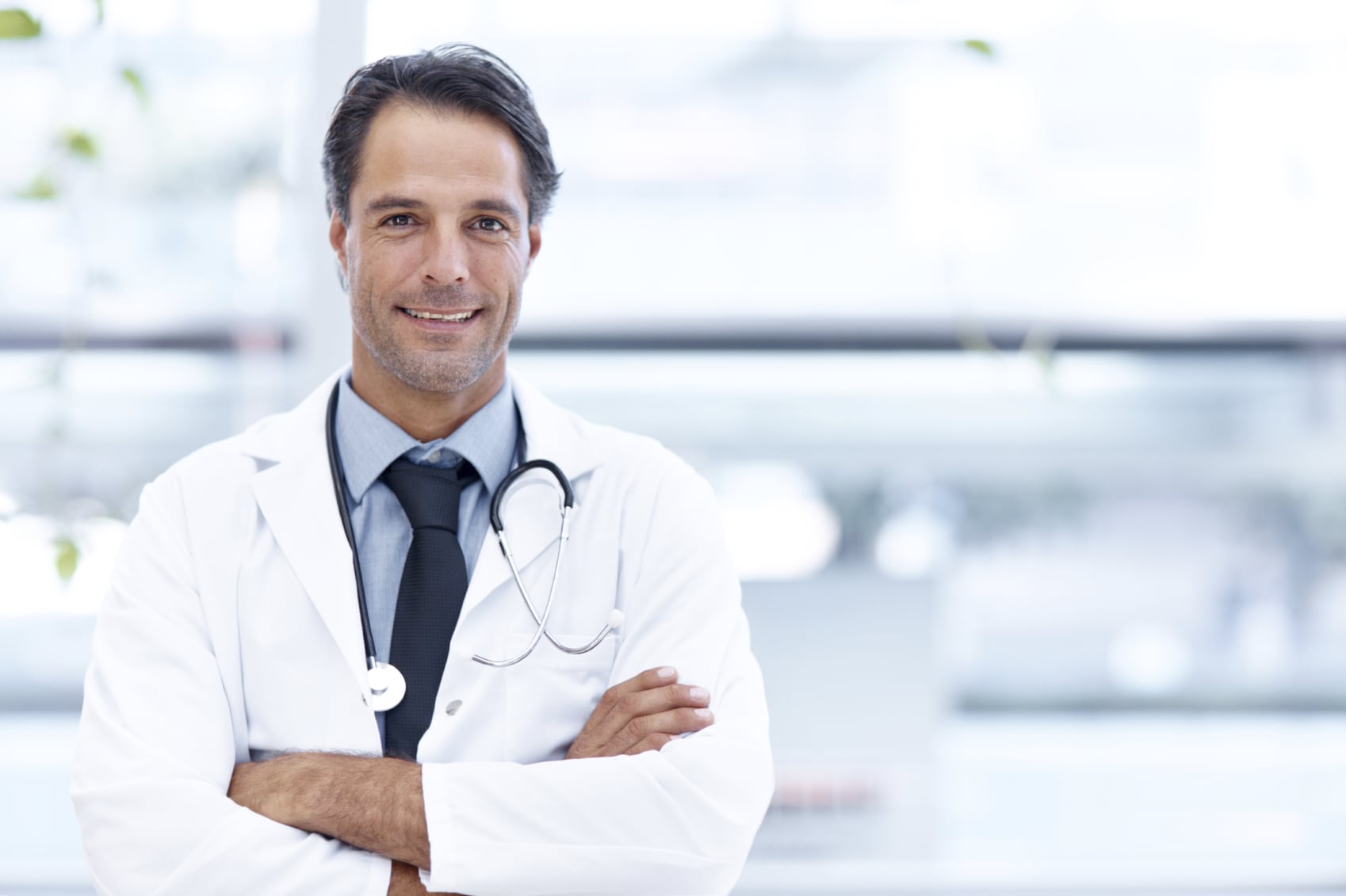 A handsome doctor standing with his arms folded and smiling at the camera - copyspace